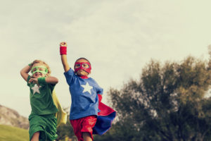 2 children dressing up as superheroes and role playing outdoors