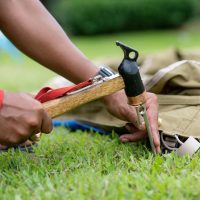 Person using a hammer to bury a tent peg in grass