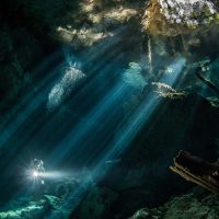light peaking through a cave with water while a diver swims